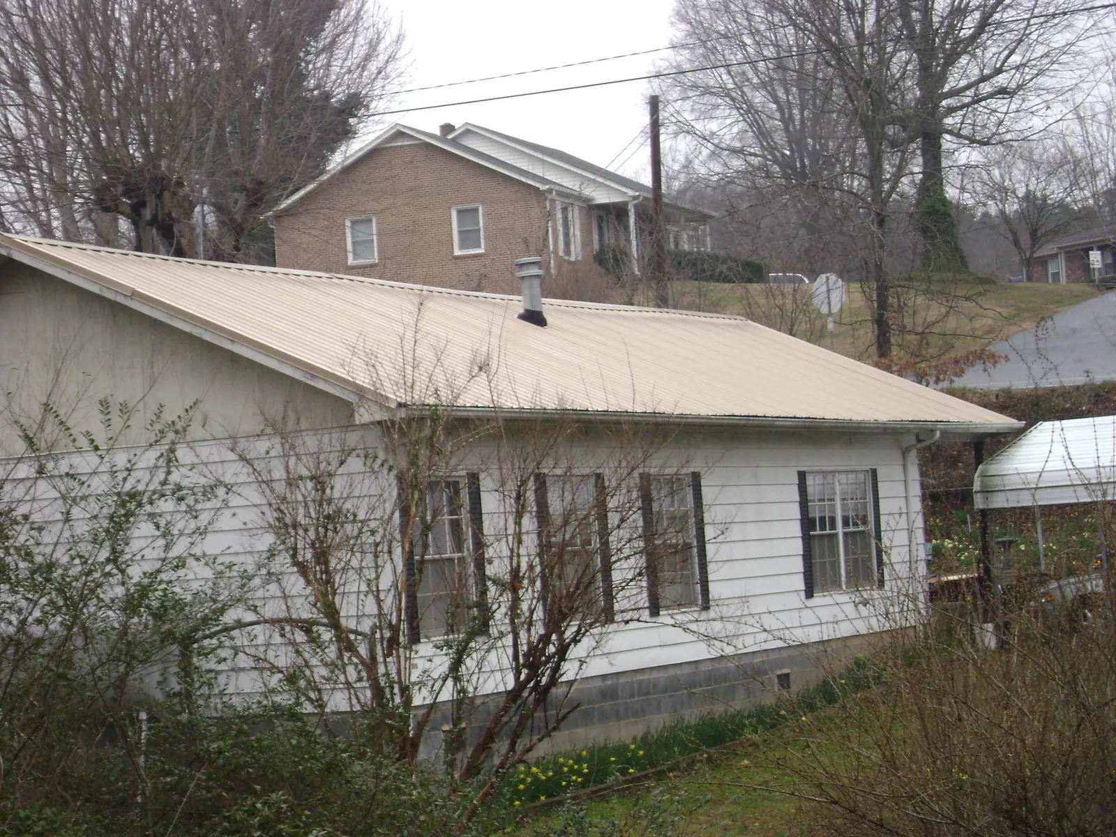 Tan metal roof on a white sided house set into a hillside — Commercial Roofing by Roofing Brothers in Spring City
